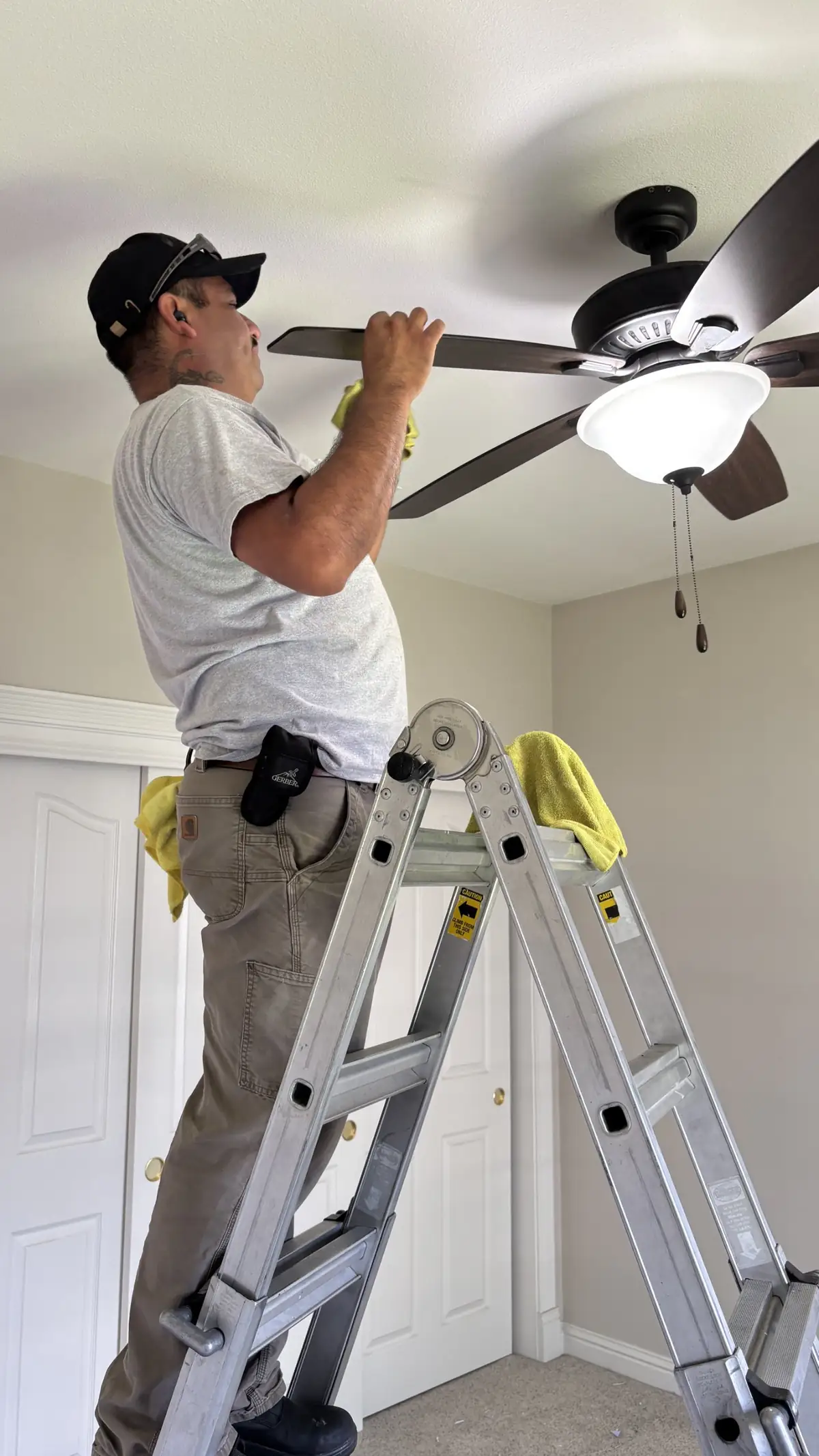 Dusting a ceiling fan from a ladder