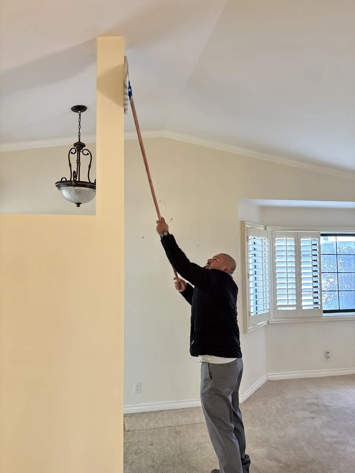 Crew member dusting ceilings and upper walls in a home after construction