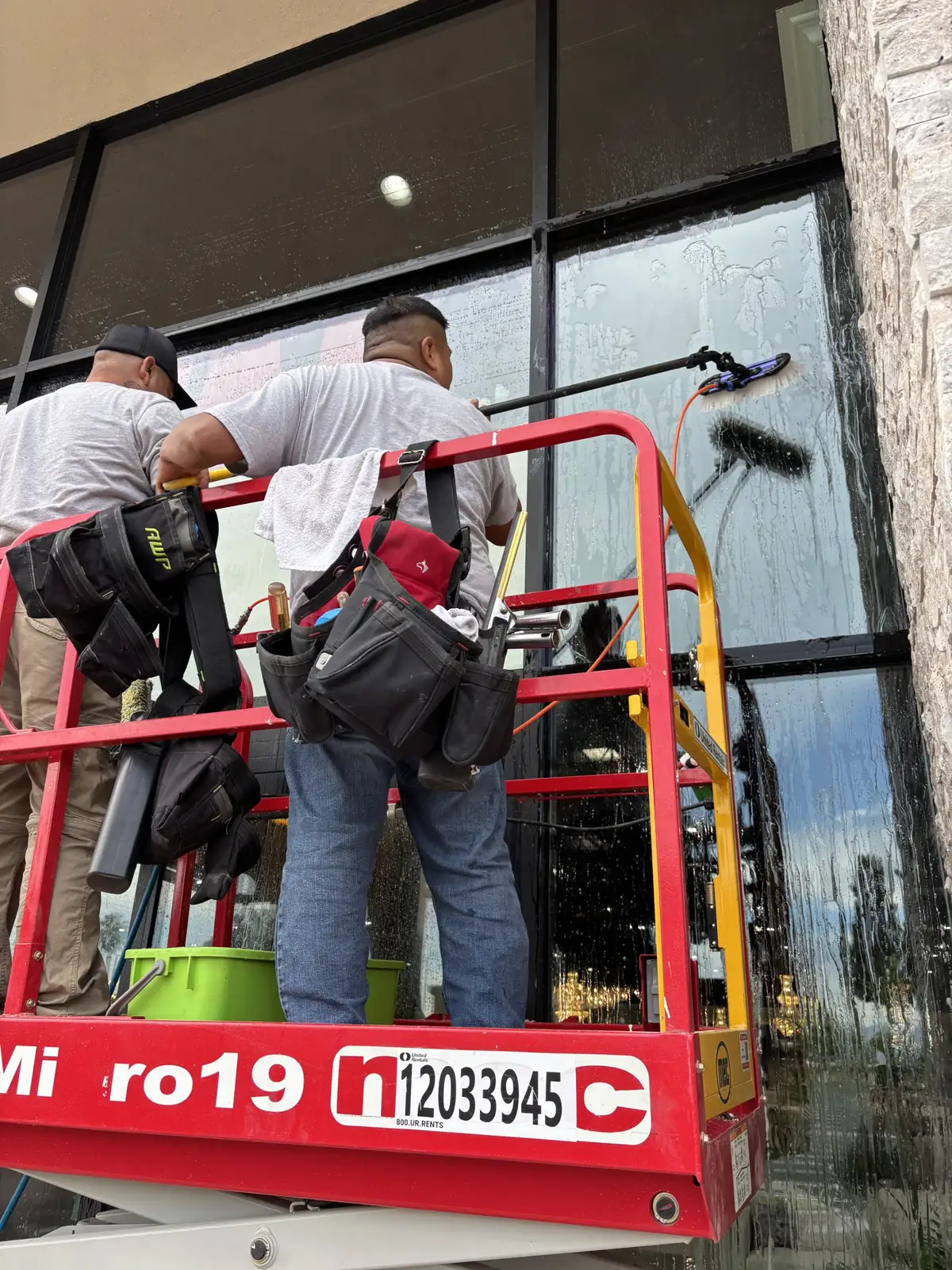 Two J&E crew members cleaning tall storefront glass from a lift