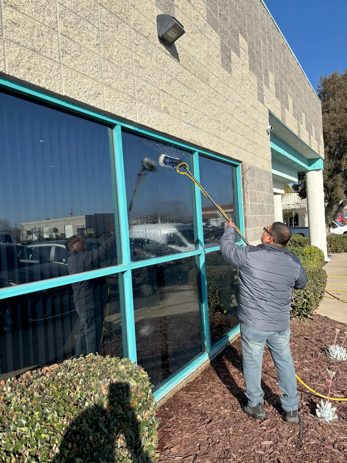 J&E technician cleaning commercial windows with a water fed pole brush
