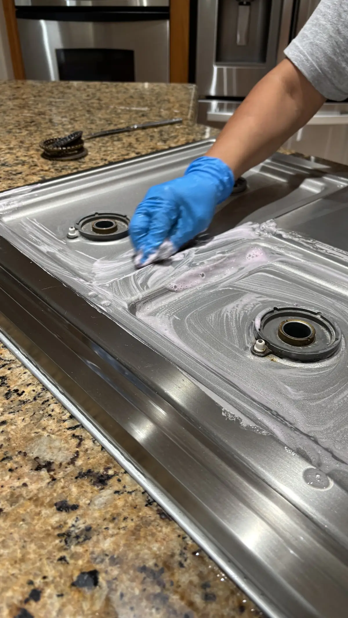 Gloved hand scrubbing grease off a stainless gas cooktop